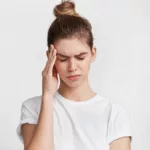 A portrait of a tired young woman rubbing her temples due to an ocular migraine