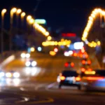 City traffic at night appearing very blurry with bright halos around all the lights depicting poor vision at night caused by night blindness